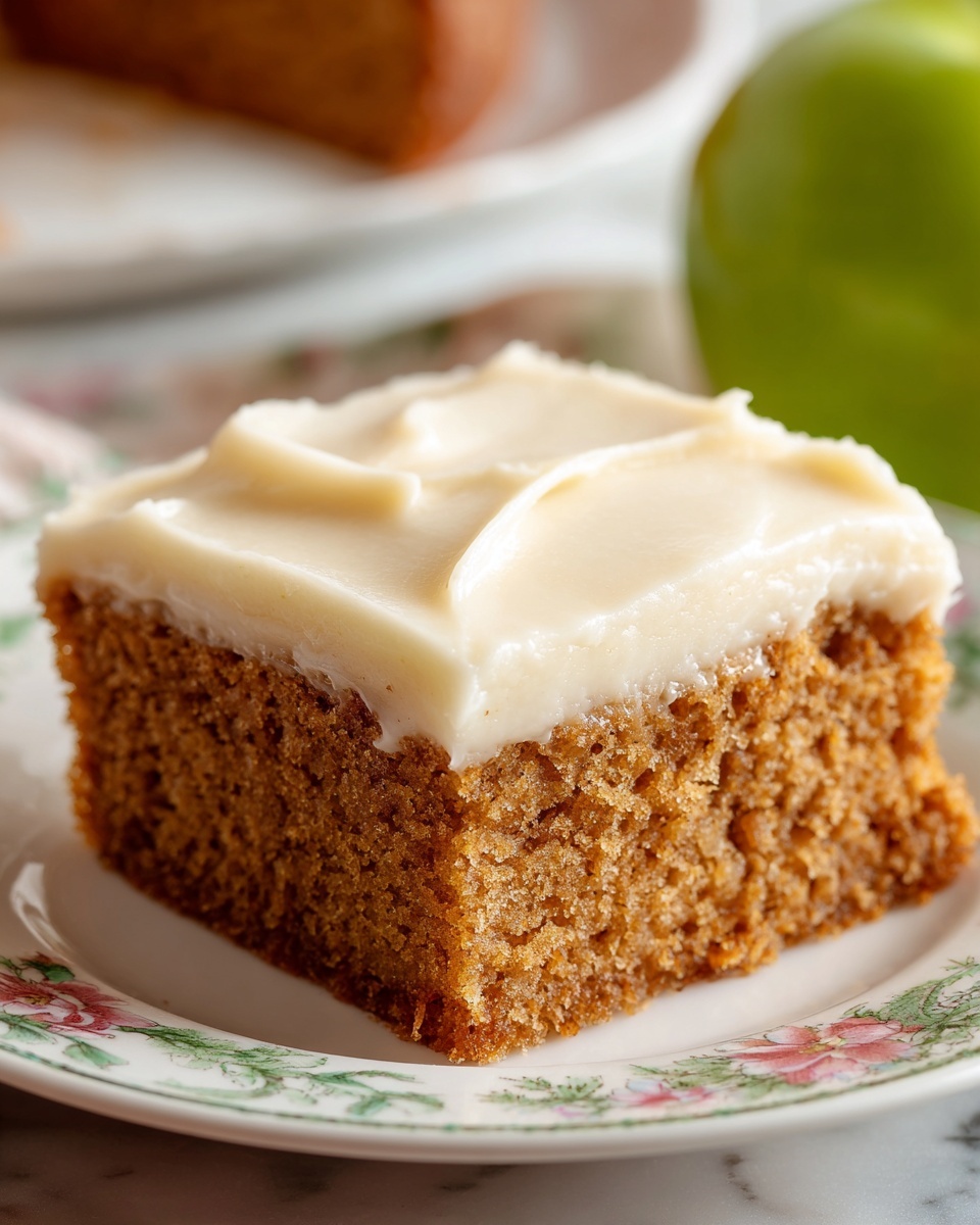 A single square piece of cake with two visible layers sits at the center of a white plate with a delicate floral pattern and a golden orange border. The bottom layer is a soft brown crumb base with a slightly rough texture, while the top layer is thick, smooth, and creamy off-white frosting spread evenly but with subtle swirls. A silver fork lies partly on the plate behind the cake. The scene is set on a white marbled surface. Photo taken with an iphone --ar 4:5 --v 7