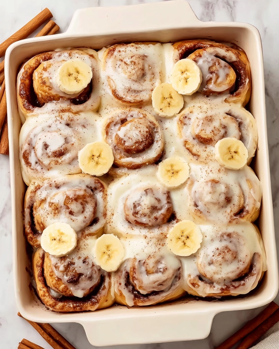 A close-up of a cinnamon roll on a white plate with a bit of thick white frosting covering the top in a spiral pattern, showing soft and fluffy light brown dough inside with a bite taken from one side. Next to the roll, there are two slices of light yellow banana placed side by side. The plate rests on a white marbled surface, with cinnamon sticks and some scattered cinnamon powder nearby, and a beige knitted cloth in the background. Photo taken with an iphone --ar 4:5 --v 7
