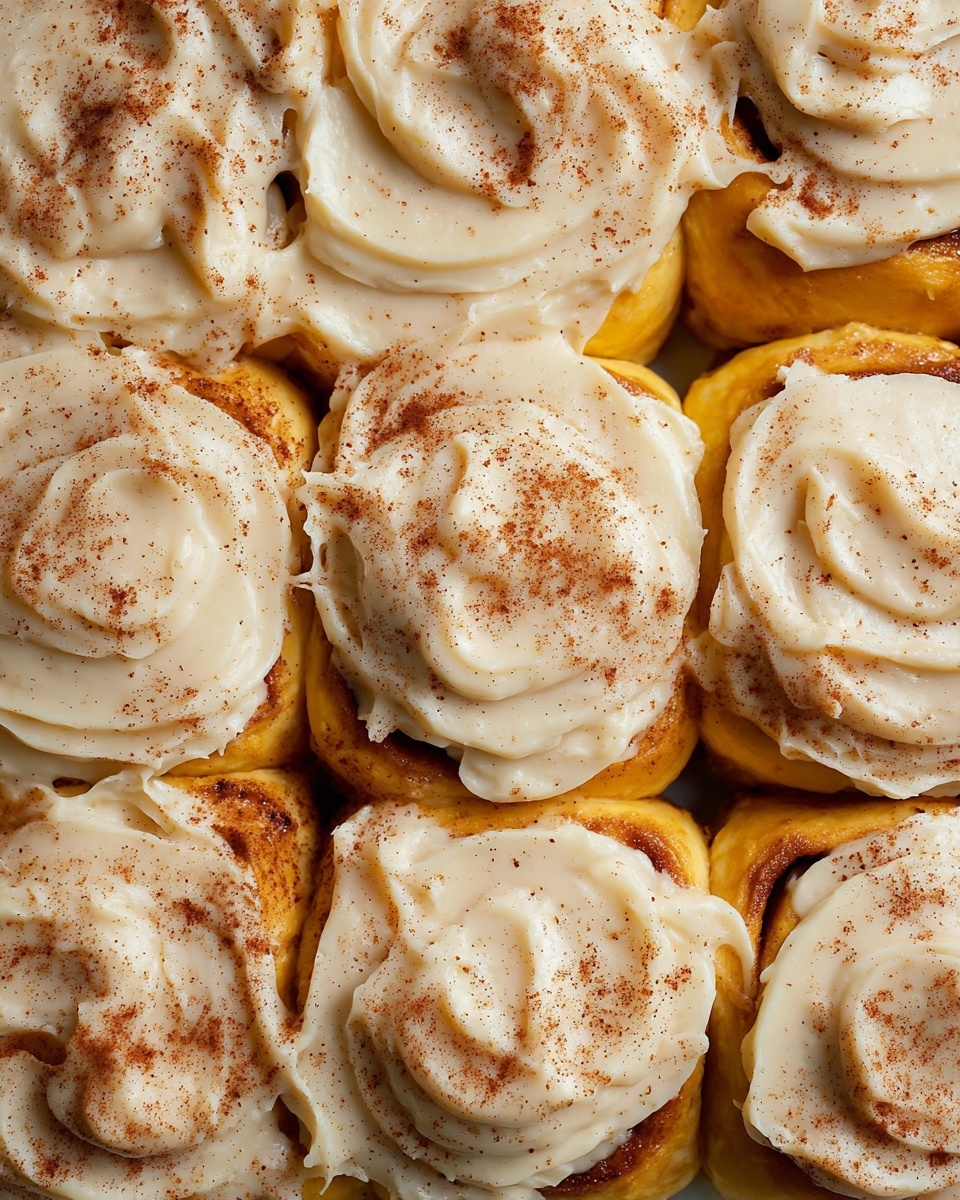 This image shows a close-up of a cinnamon roll with three visible layers. The base layer is a dark golden brown soft dough with some caramelized cinnamon spots. Above that, there is an orange-brown inner dough swirl with a soft, fluffy texture. The top layer is thick white cream cheese frosting generously spread over the roll, with a smooth and slightly uneven texture, sprinkled lightly with ground cinnamon powder. A golden spoon with some frosting and cinnamon roll crumbs rests on the edge of the white plate, which sits on a white marbled surface. Photo taken with an iphone --ar 4:5 --v 7
