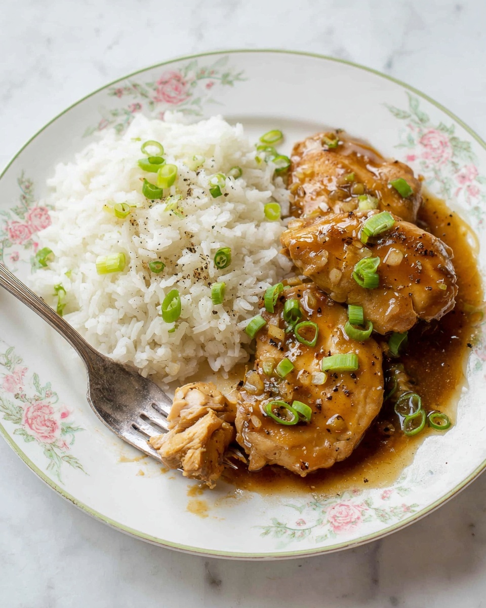 The image shows a white plate with a light floral pattern filled with two main layers: a portion of white rice on the top half, sprinkled with small green onion pieces and black pepper, and below it, two smooth, brown glazed pieces of meat covered in a shiny brown sauce, garnished with green onion slices. A silver fork lies on the right side of the plate resting partly on the rice. The plate sits on a white marbled surface with a white cloth napkin on the left side. Photo taken with an iphone --ar 4:5 --v 7