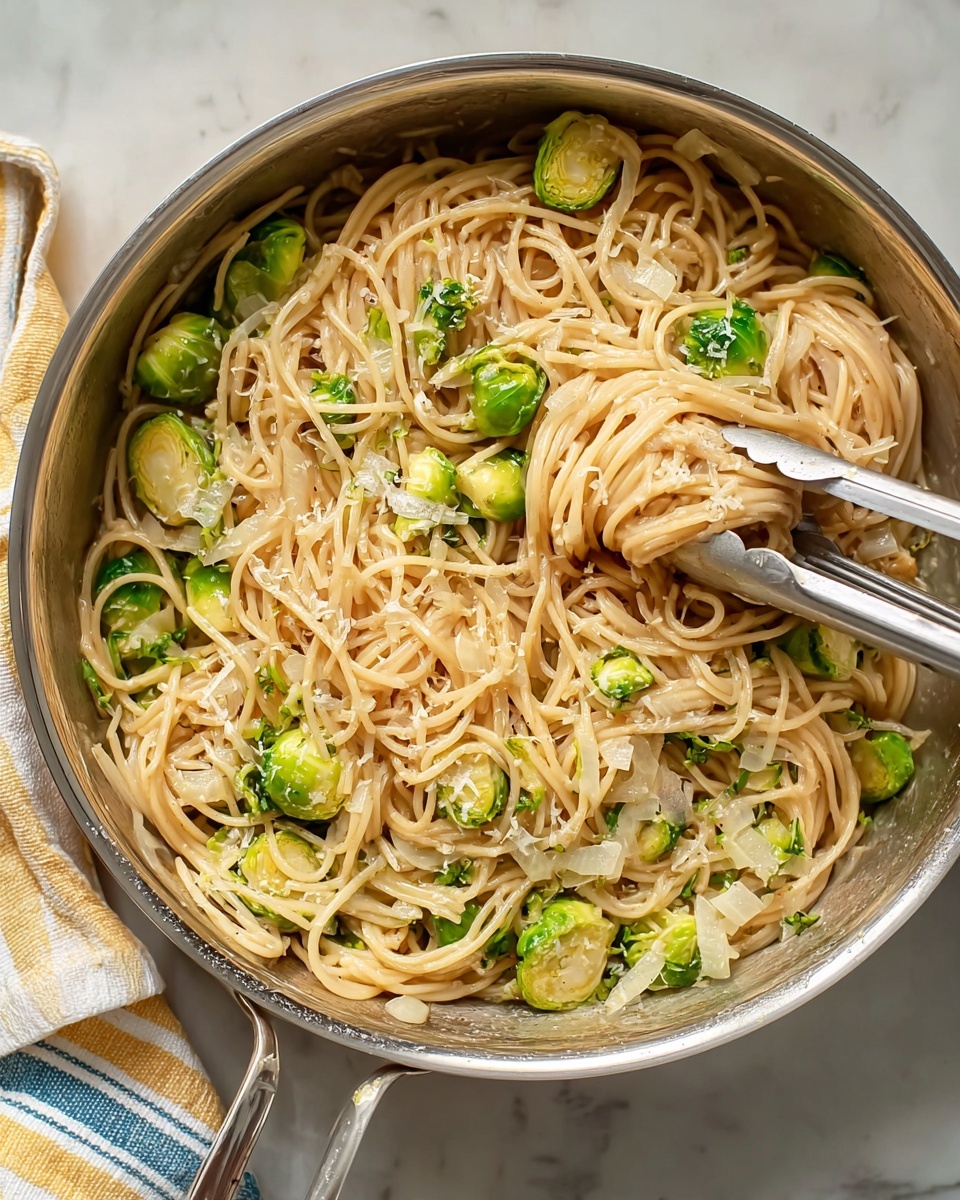 The image shows a metal pan filled with spaghetti noodles mixed with halved green Brussels sprouts and small pieces of white onions. The noodles are creamy light brown in color, swirling around the Brussels sprouts. A pair of silver tongs lifts a portion of the spaghetti from the pan, with a few Brussels sprout pieces clinging to the noodles. The pan sits on a white marbled surface, and striped cloths with soft yellow and blue lines are partially visible to the side. The overall scene is bright and simple, highlighting the warm pasta dish. photo taken with an iphone --ar 4:5 --v 7