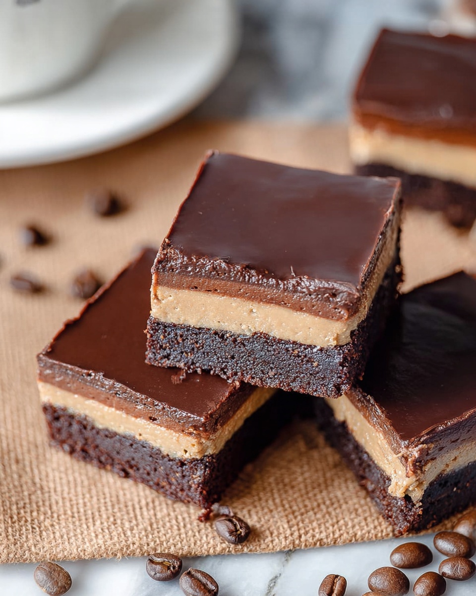 The image shows three square chocolate dessert pieces placed on a brown textured surface with scattered coffee beans around. Each dessert has three visible layers: a bottom dark chocolate cake layer with a moist, dense texture; a thin, light tan creamy middle layer; and a thick, smooth dark chocolate top layer with a shiny finish. One piece is tilted, showing all layers clearly from the side, while the other two pieces rest flat, highlighting the glossy top. The background includes a blurred white marbled texture and part of a white plate at the edge. photo taken with an iphone --ar 4:5 --v 7