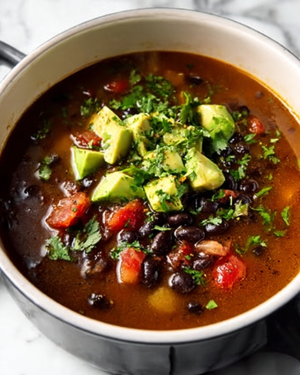 Single white bowl filled with a warm serving of black bean soup, showcasing a rich broth with visible black beans, diced tomatoes, and finely chopped onions, topped with vibrant avocado chunks and freshly chopped cilantro, close-up angled shot capturing the textures and fresh garnishes, steam gently rising, placed on white marble surface, intimate plated serving photo taken with an iphone --ar 4:5 --v 7