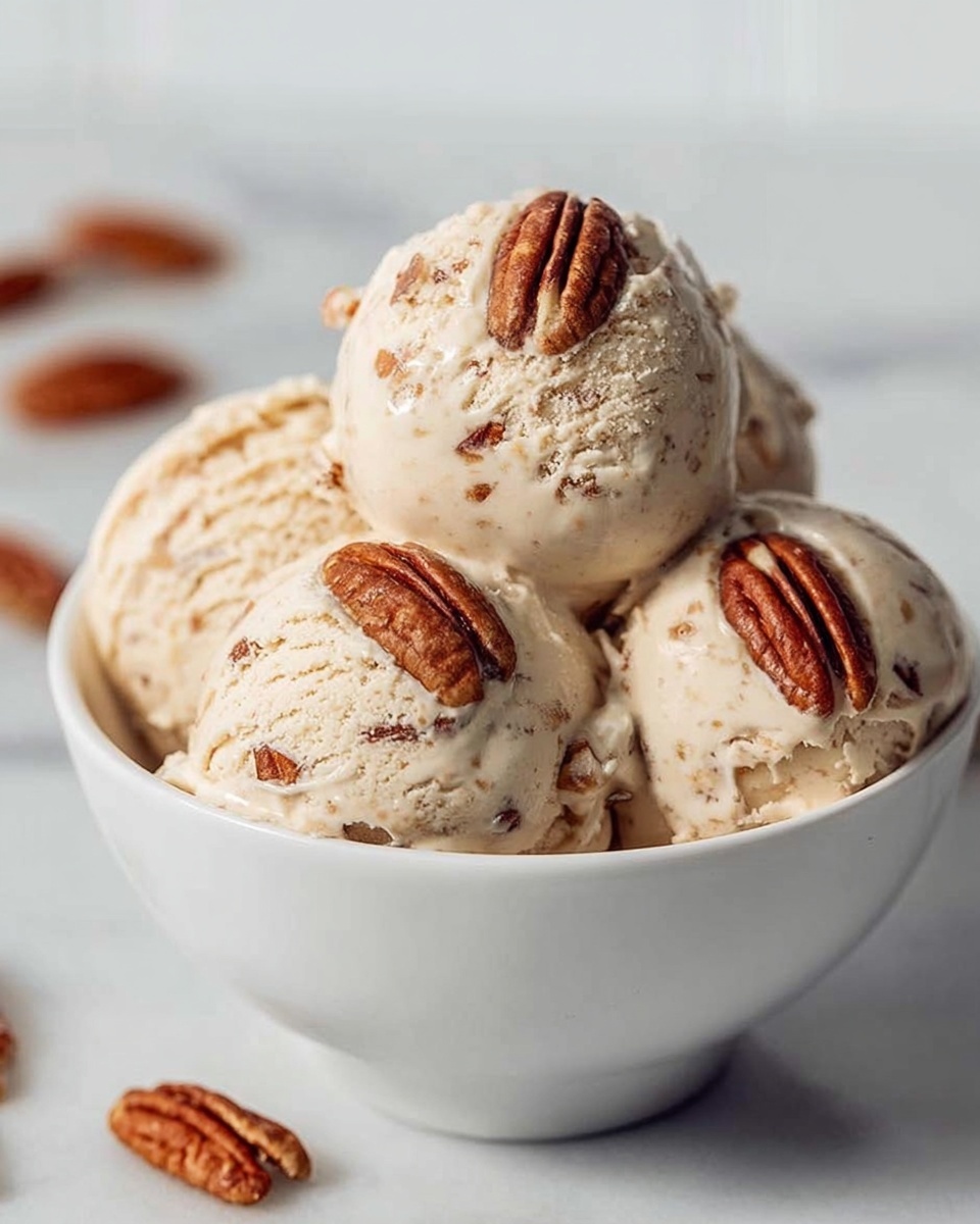 A white bowl holds four round scoops of light tan ice cream with small brown bits inside, each scoop topped with a whole pecan. The ice cream has a creamy texture with visible specks, and the pecans add a rich brown, wrinkled contrast on top. The bowl sits on a white marbled surface, with a few pecans scattered blurred in the background. The overall scene is bright and clean, with soft lighting highlighting the smoothness of the ice cream. photo taken with an iphone --ar 4:5 --v 7