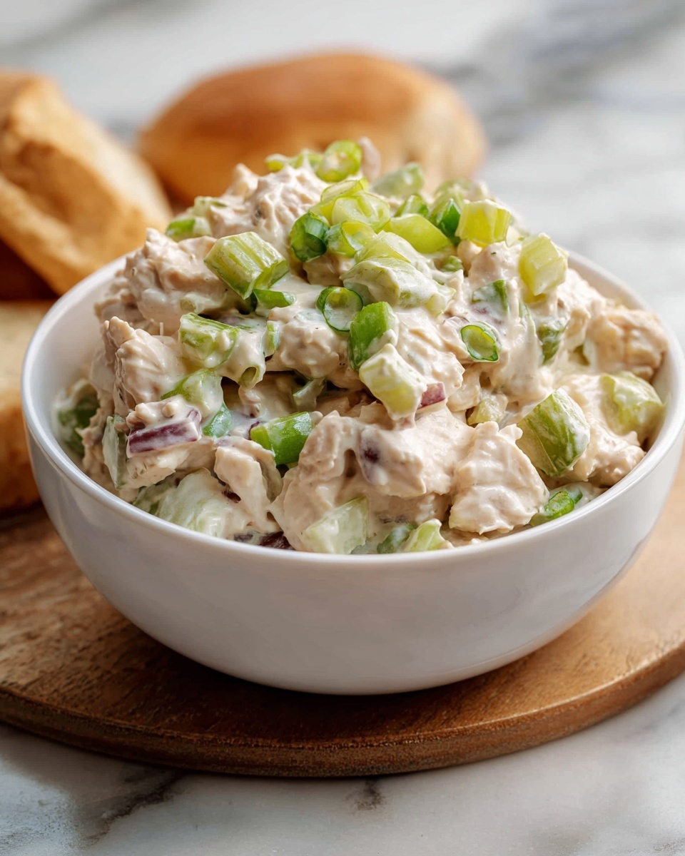 A white marble countertop featuring a large white serving platter heaped with multiple creamy chicken salad sandwiches on soft, golden brioche buns, filled generously with diced tender chicken, crunchy celery, and a light mayonnaise dressing, accompanied by a white bowl brimming with extra chicken salad, all presented in natural lighting with professional food styling, whole dish photographed from a 3/4 angle --ar 4:5 --v 7