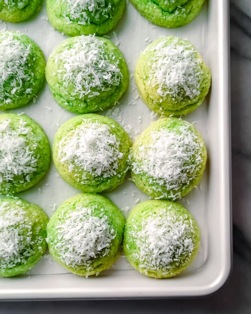 White rectangular baking tray filled with freshly baked bright green pandan cookies, each topped generously with fluffy shredded coconut, cookies arranged neatly in rows covering the entire tray, the surface slightly textured and soft-looking, photographed with natural light from a 3/4 angle, placed on a white marble countertop, professional food styling, photo taken with an iphone --ar 4:5 --v 7