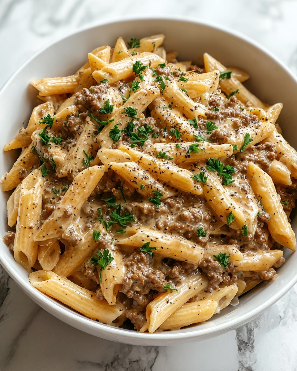 Large white serving bowl filled with creamy penne pasta mixed generously with browned ground beef, coated with a rich, velvety white sauce and sprinkled with finely chopped fresh parsley, the whole dish presented from a top-down 3/4 angle, resting on a pristine white marble countertop under natural light, styled as a professional hero shot from a food magazine, photo taken with an iphone --ar 4:5 --v 7