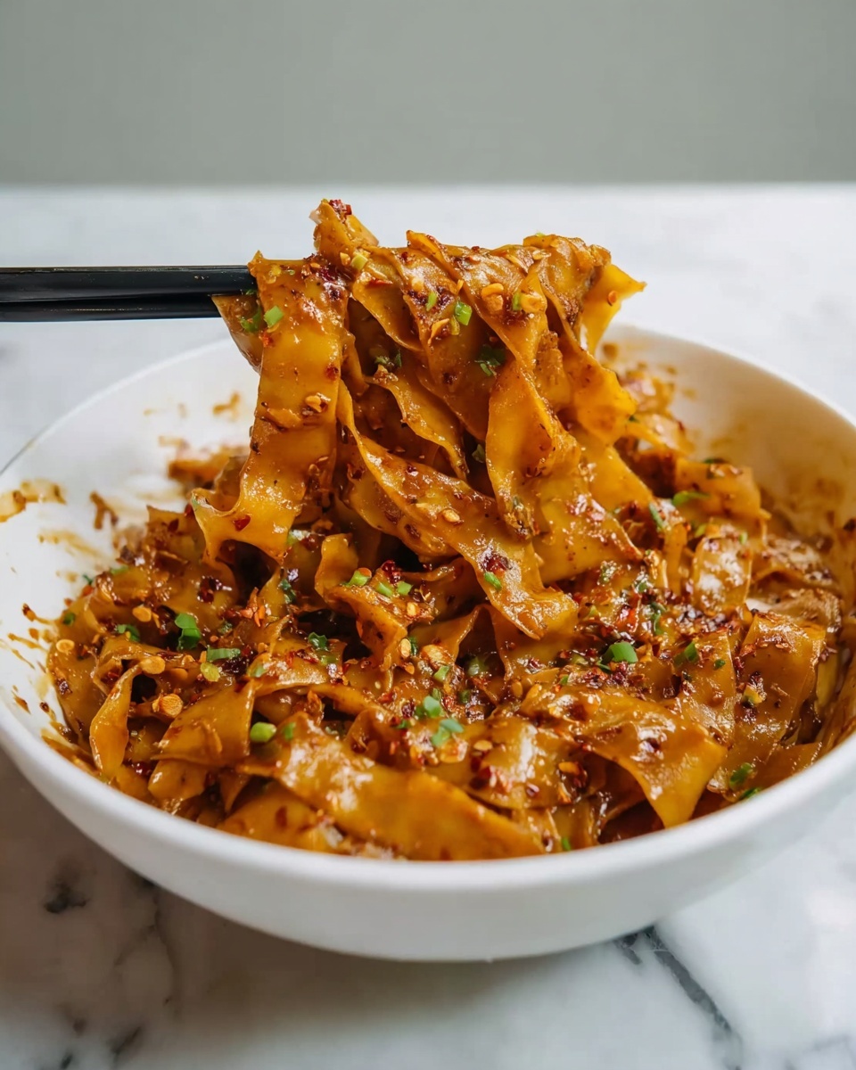 Cilantro Lime Noodles Recipe 6 Large white bowl filled with a generous serving of ruffled, wide noodles tossed in a rich, savory sauce speckled with fresh green herbs, the noodles glistening under natural light on a pristine white marble countertop, shot from a 3/4 angle to showcase the full bowl and its glossy texture, professional food styling photo taken with an iphone --ar 4:5 --v 7