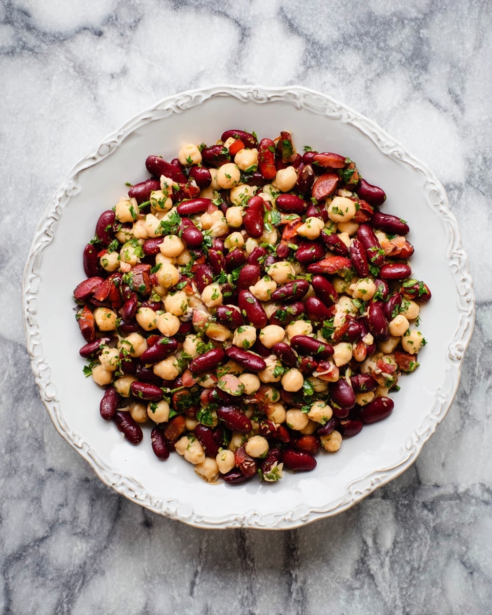 Large white ornate serving bowl filled with a vibrant mixed bean salad featuring whole red kidney beans and pale chickpeas, lightly seasoned and garnished with finely chopped fresh herbs, photographed from above with the entire bowl in frame on a white marble countertop under natural lighting, professional food magazine style hero shot photo taken with an iphone --ar 4:5 --v 7