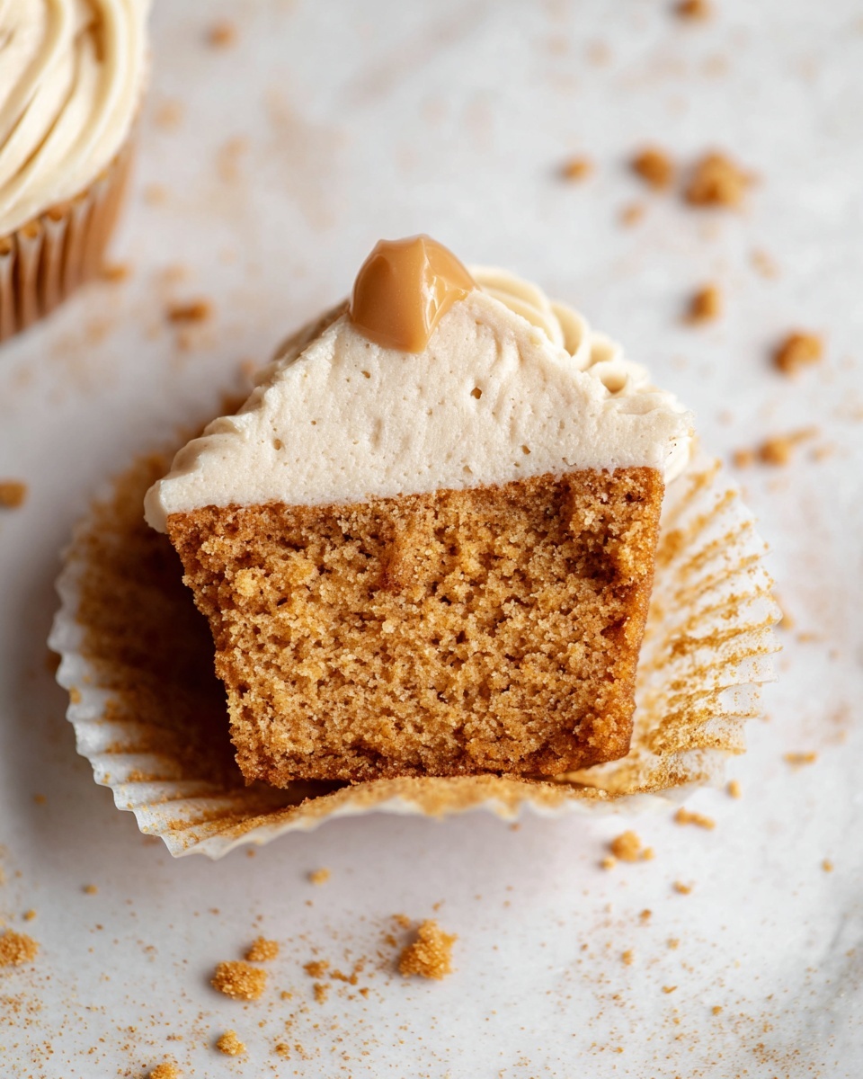 A white rectangular platter filled with a dozen perfectly frosted Lotus Biscoff cupcakes, each topped with smooth, swirled caramel-colored frosting, a dollop of rich Biscoff spread in the center, and decorated with drizzles of caramel sauce and sprinkled crushed Biscoff cookie crumbs, crumbs and broken cookie pieces artfully scattered around on a white marble countertop, natural lighting highlighting the texture and colors, professional food magazine hero shot photo taken with an iphone --ar 4:5 --v 7