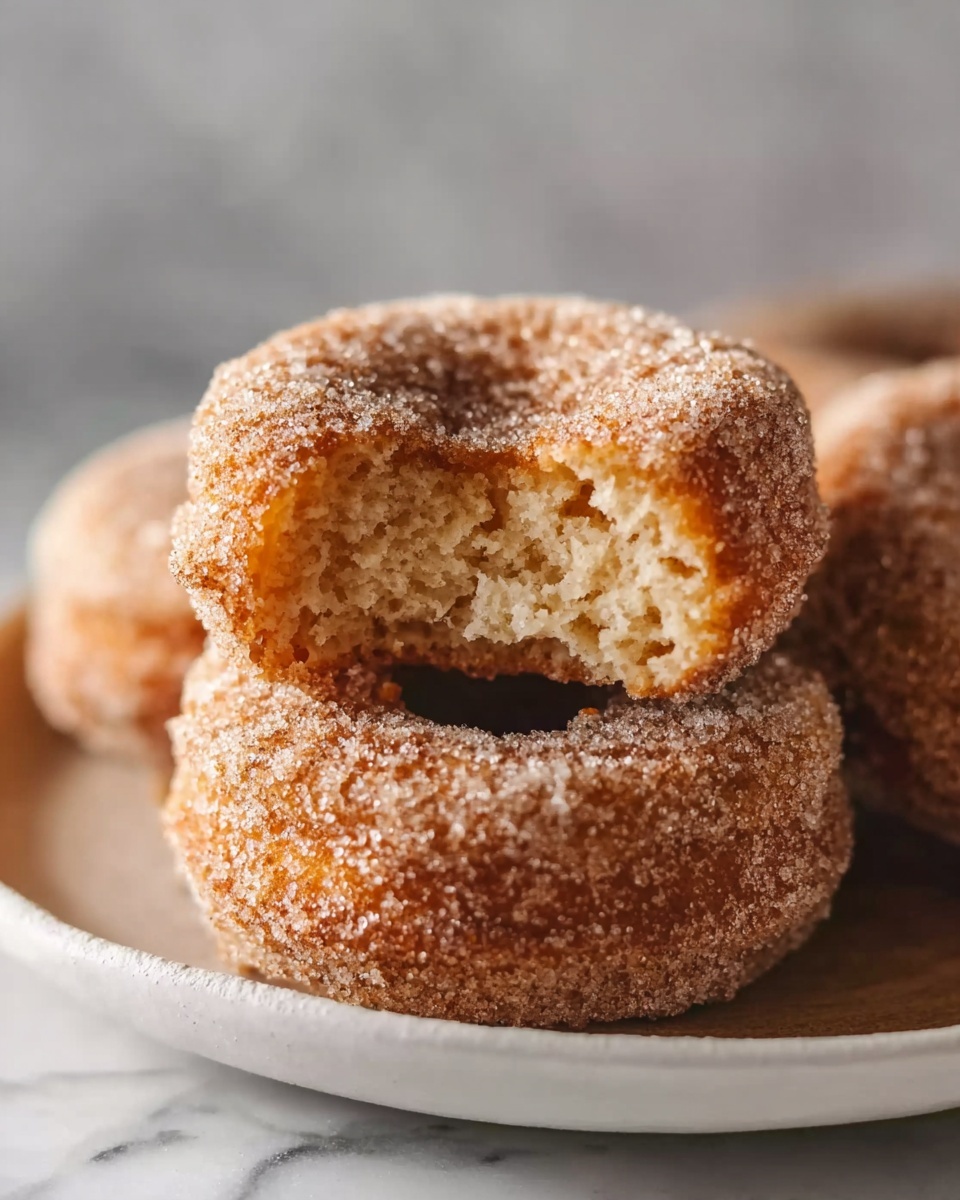 Fluffy Banana Bread Donuts Recipe 6 A large white rectangular platter filled with an entire batch of freshly baked cinnamon sugar donuts, each perfectly round with a golden-brown crust coated in a generous layer of cinnamon sugar, arranged neatly and overlapping slightly to showcase their fluffy texture and warm, inviting appearance; the warm natural lighting enhances the sugary sparkle on each donut, shot from a close 3/4 angle to capture the full, uncut batch on a clean white marble surface, professional food styling photo taken with an iphone --ar 4:5 --v 7