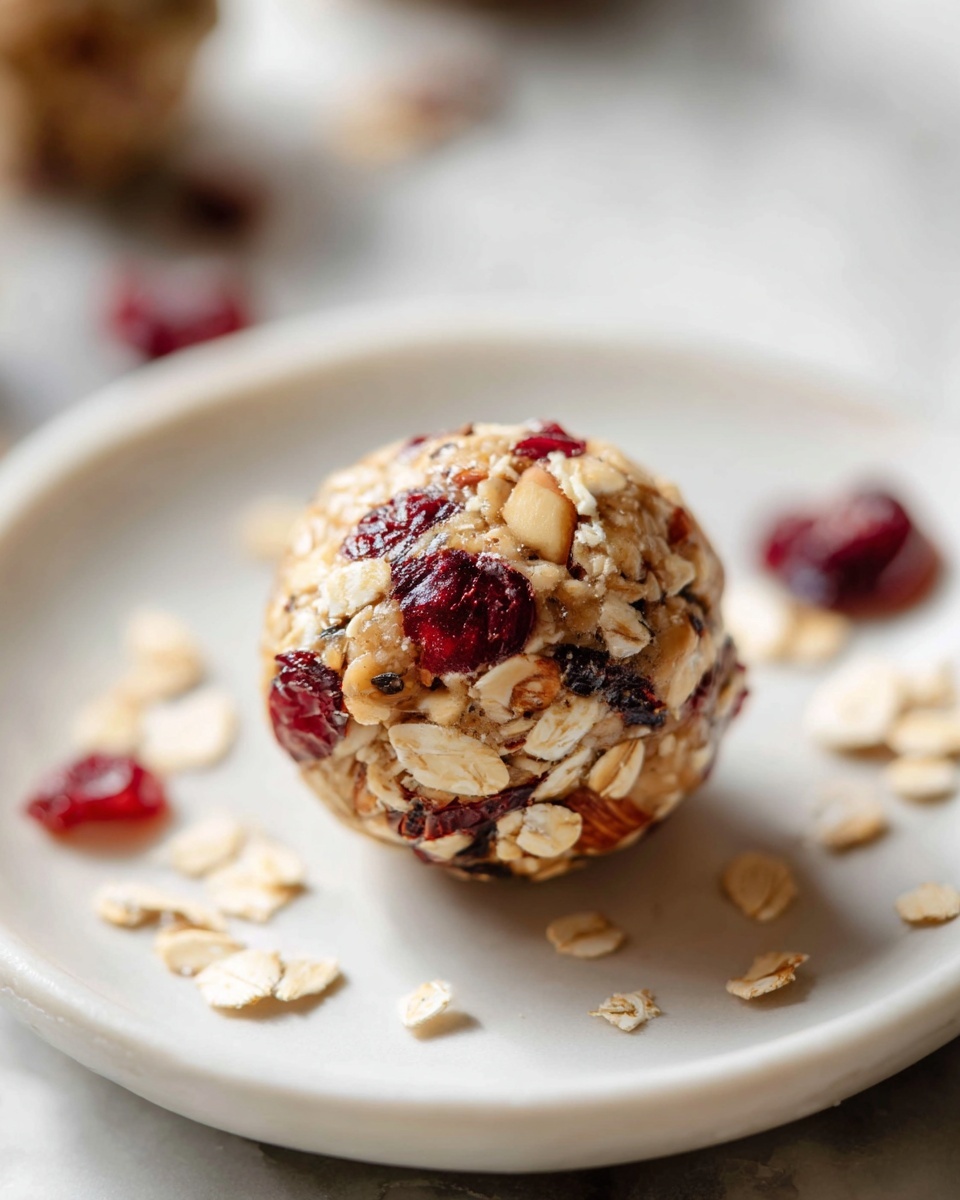 Large white serving platter filled with an abundant arrangement of no-bake energy balls packed with cranberries, oats, chia seeds, and almond slivers, each round bite-sized ball visibly textured and studded with vibrant red cranberries, all presented together to highlight their wholesome, hearty ingredients, photographed from a slight 3/4 angle on a white marble countertop with natural lighting, professional food magazine style photo taken with an iphone --ar 4:5 --v 7