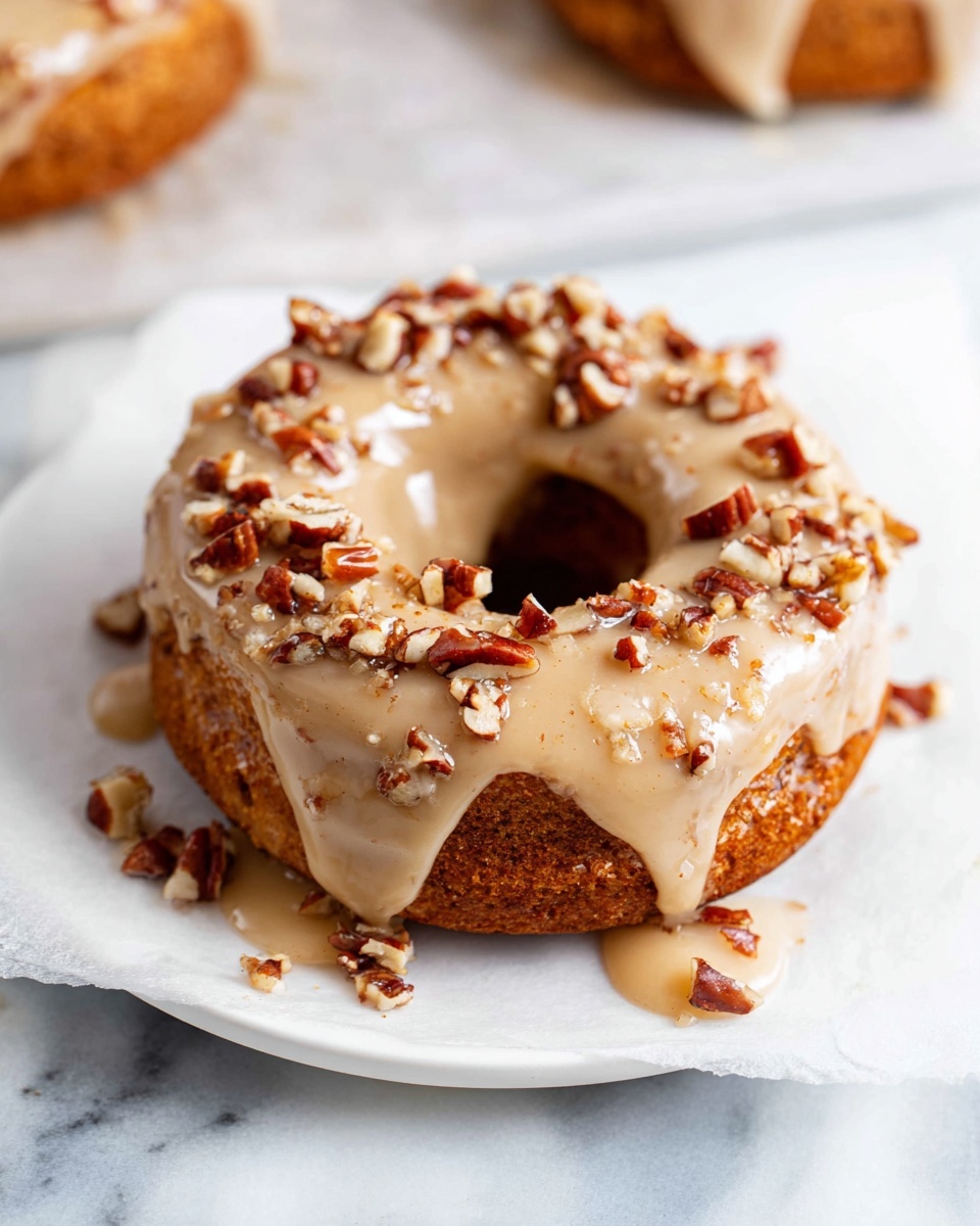 Pumpkin Spice Donuts with Maple Icing {Paleo, Gluten Free} Recipe 6 A white platter artfully arranged with a full batch of freshly baked pumpkin spice doughnuts, each doughnut generously drizzled with smooth, creamy maple glaze and sprinkled with chopped toasted pecans, showcasing the warm, golden-brown texture of the doughnuts under natural lighting, captured from a 3/4 angle against a pristine white marble background in a professional food magazine hero shot, photo taken with an iphone --ar 4:5 --v 7