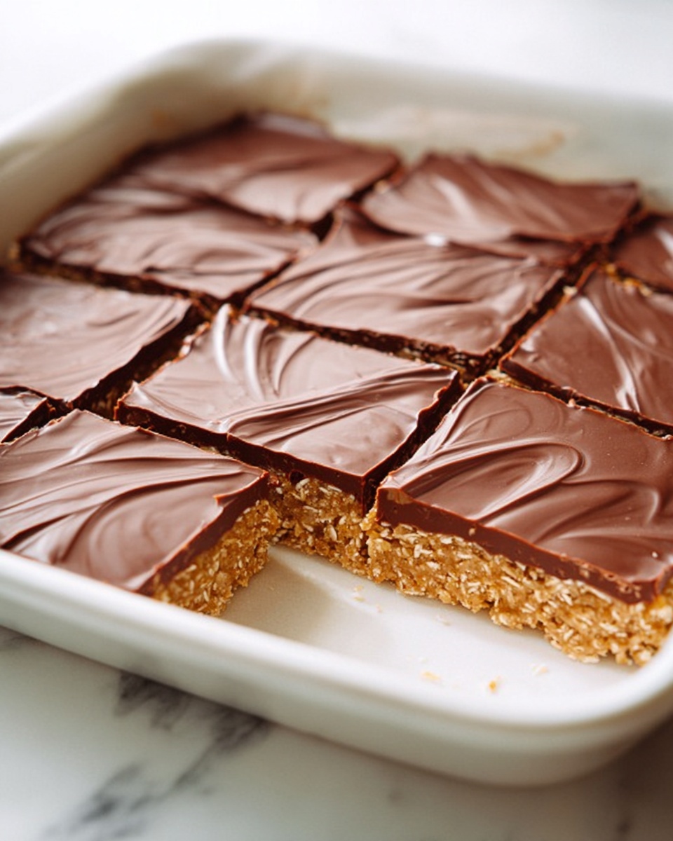 Large white rectangular baking dish filled with an entire homemade no-bake chocolate oat square bar dessert, showcasing a thick golden oat base topped with a smooth, glossy layer of rich dark chocolate, with delicate swirl patterns on the chocolate surface, photographed from a three-quarter angle on a white marble countertop with natural lighting, professional food styling photo taken with an iphone --ar 4:5 --v 7