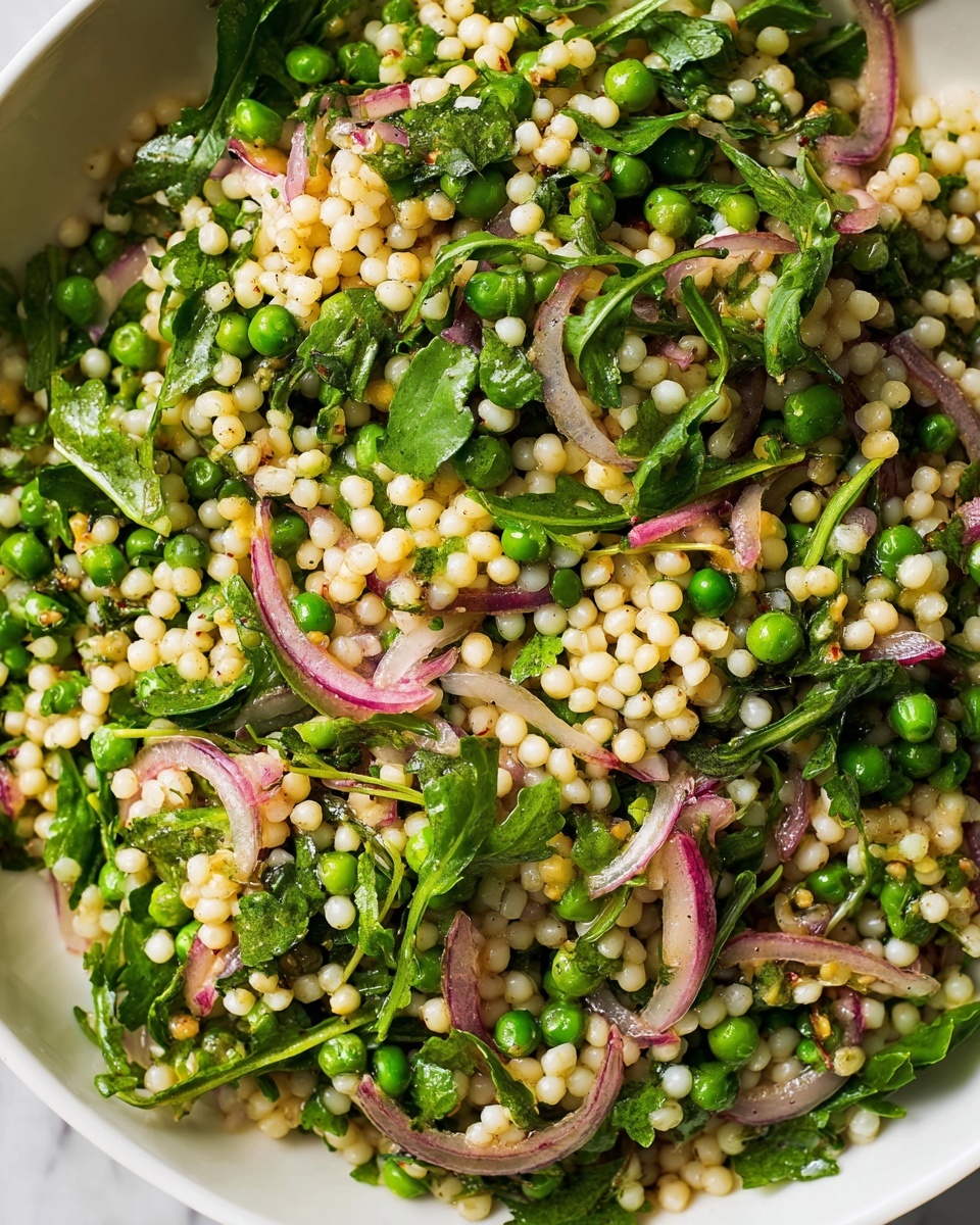 Large white bowl filled with a fresh and vibrant pearl couscous salad, featuring a generous mix of bright green peas, crisp arugula, thinly sliced red onions, and fresh mint leaves, all tossed lightly with herbs and seasoning, shot in natural lighting on a white marble background from a 3/4 angle to showcase the entire wholesome dish, professional food magazine style hero shot photo taken with an iphone --ar 4:5 --v 7
