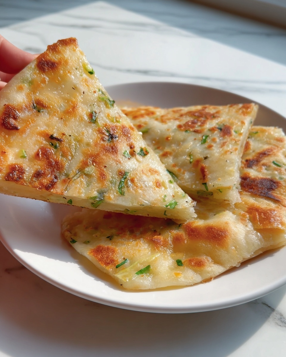 Three whole, golden-brown scallion pancakes stacked slightly overlapping on a large white plate, each pancake showcasing the crispy, bubbly surface speckled with fresh green scallion bits, photographed from a 3/4 angle on a white marble countertop under natural lighting, styled like an appetizing hero shot from a food magazine, photo taken with an iphone --ar 4:5 --v 7