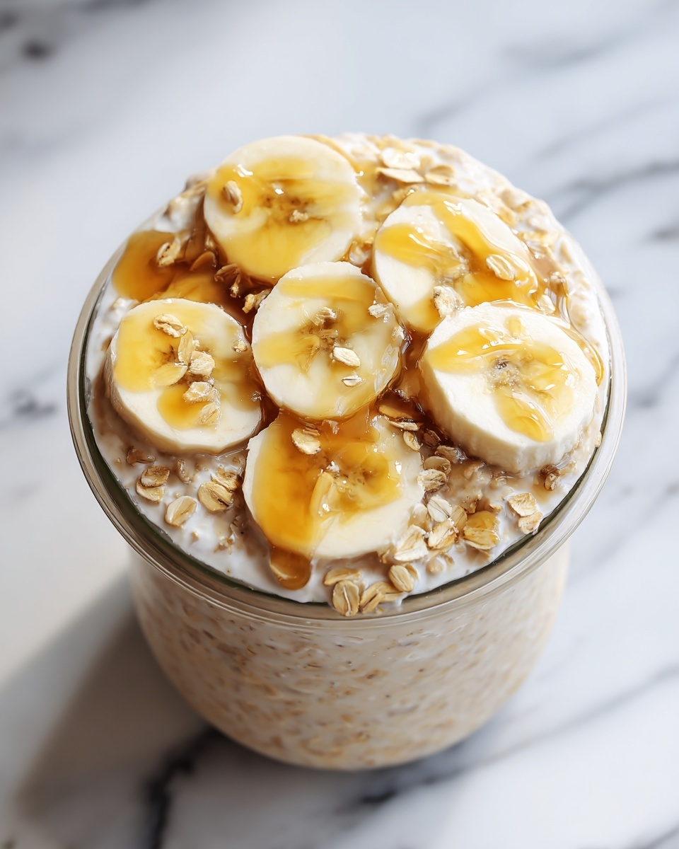 A large white bowl filled to the brim with creamy overnight oats topped generously with fresh banana slices arranged in a circular pattern, all drizzled with golden maple syrup, surrounded by scattered oat flakes on a white marble countertop, whole dish captured in a professional 3/4 angle food magazine style photo taken with an iphone --ar 4:5 --v 7