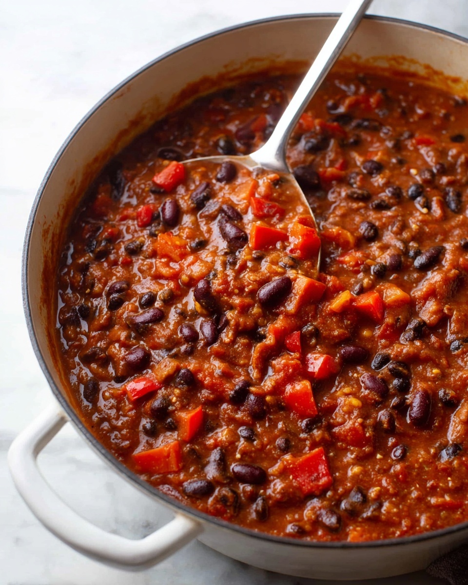Large white saucepan filled with rich, hearty chili featuring an abundance of black and kidney beans, diced red bell peppers, and a thick tomato-based sauce, showing the full dish with a shiny ladle resting inside, photographed from a 3/4 angle on a white marble countertop with natural lighting, professional food styling photo taken with an iphone --ar 4:5 --v 7