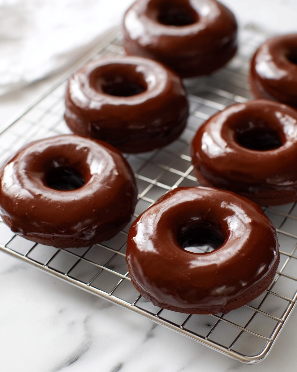 A white ceramic platter filled with a full batch of six perfectly round chocolate-glazed donuts, each donut featuring a smooth, shiny, and evenly coated chocolate icing that gleams under natural light, arranged neatly on a cooling rack atop a pristine white marble countertop, captured from a 3/4 angle with professional food styling, emphasizing the rich, indulgent texture of the donuts, photo taken with an iphone --ar 4:5 --v 7