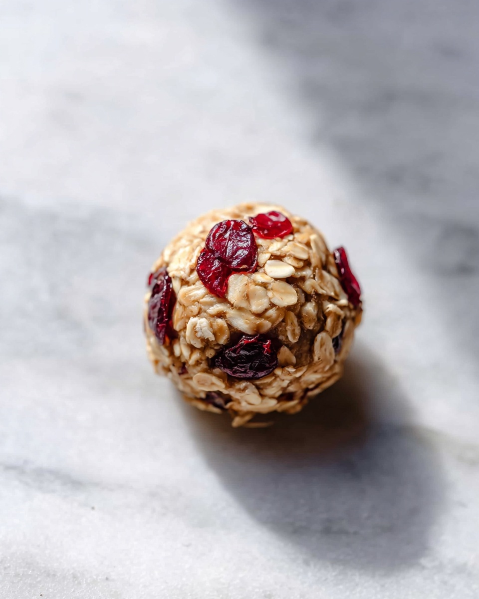 A large white ceramic bowl completely filled with round oatmeal energy bites, each studded generously with dried cranberries and visible rolled oats, arranged in an abundant mound showing their textured and wholesome ingredients, accompanied by scattered dried cranberries around the bowl, all placed on a white marble countertop under soft natural lighting, professional food styling, photo taken with an iphone --ar 4:5 --v 7